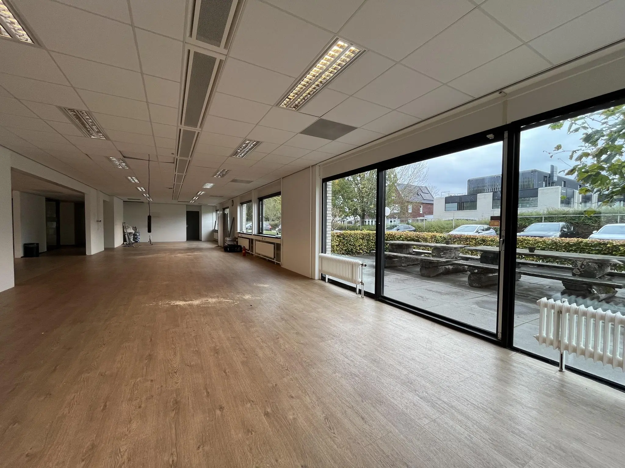 Leegstaand kantoorruimte aan de Burgemeester Verderlaan met grote ramen en uitzicht op een parkeerplaats en straat.